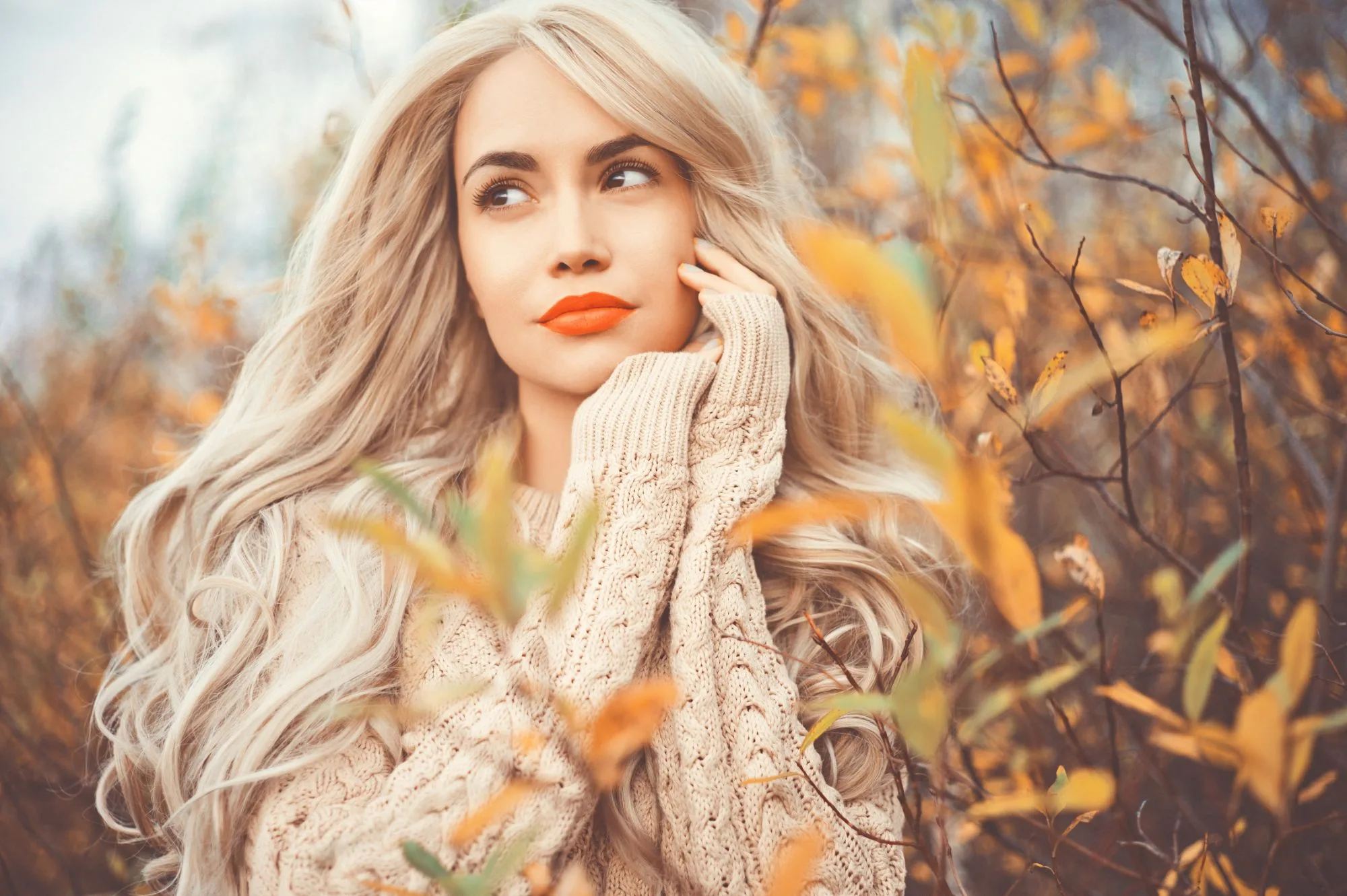 Woman in a cozy knit sweater surrounded by autumn leaves